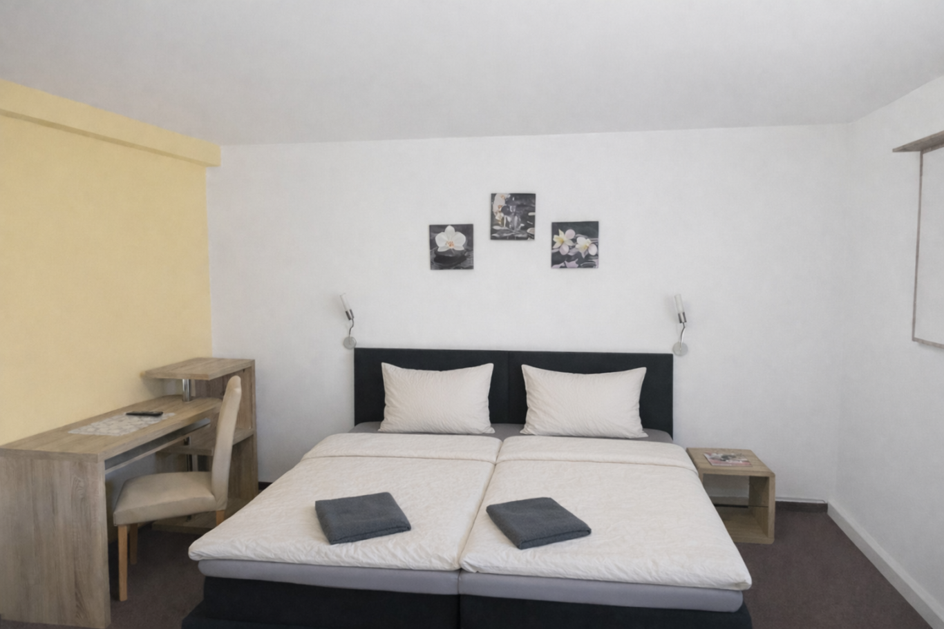 Helles Zimmer mit Doppelbett, Schreibtisch und modernen Wandbildern.