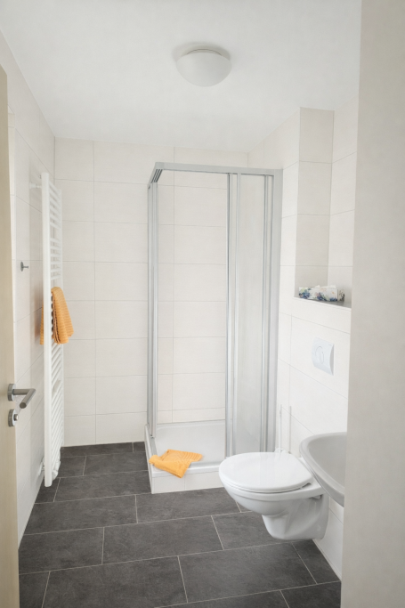 Helles Bad mit Dusche, WC und Handtuchhalter in neutralen Farben.