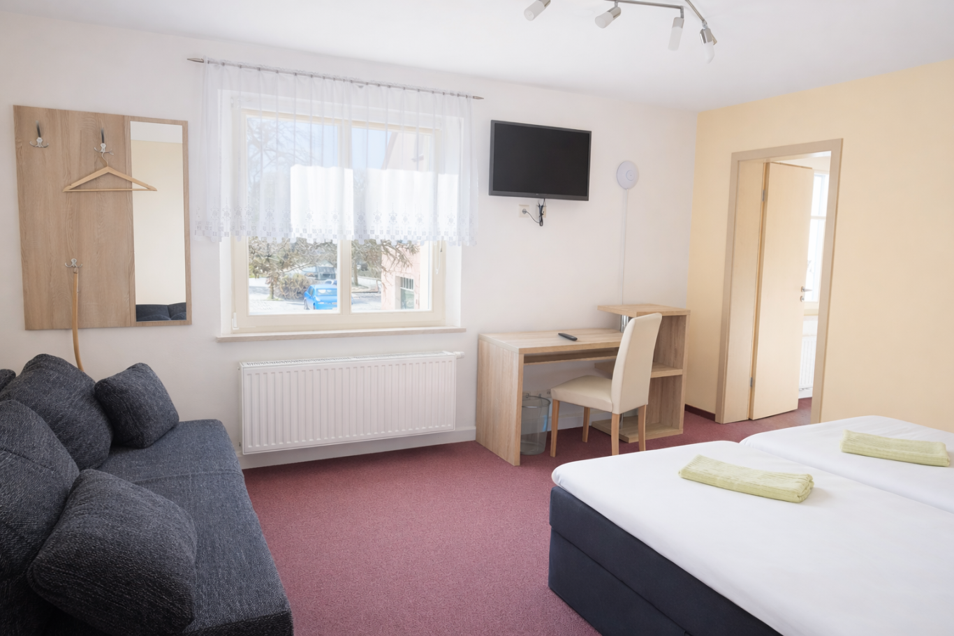 Helle Hotelzimmer mit zwei Betten, Sofa, Schreibtisch und Fenster zur Aussicht.