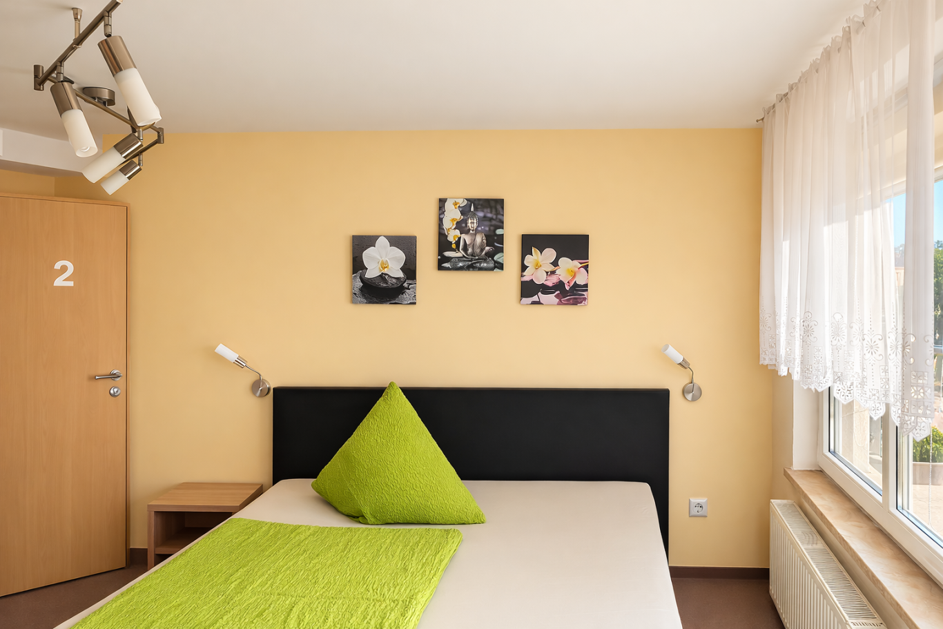 Heller Schlafraum mit einem Bett, grüner Kissen und Bildern an der Wand.