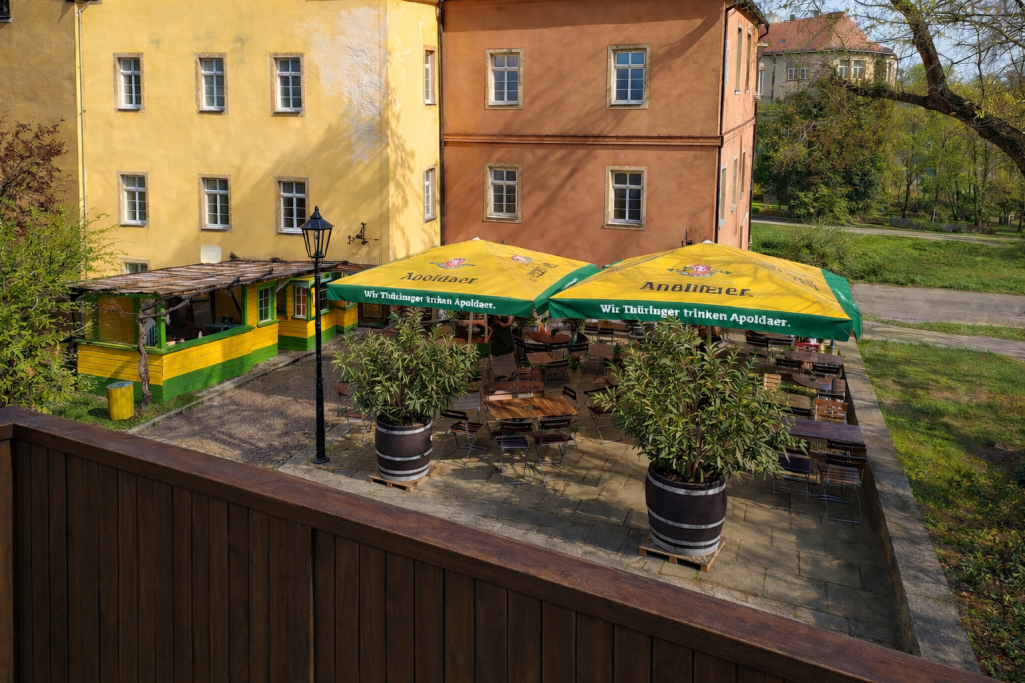 Sonniger Außenbereich eines Restaurants mit gelben Sonnenschirmen und Bäumen.
