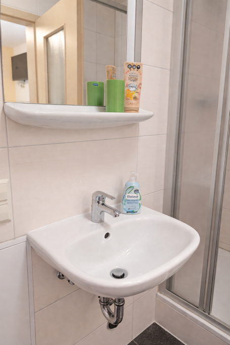 Waschbecken mit Seife und Pflegeprodukten auf einem Regal in einem Badezimmer.