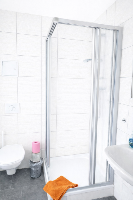 Moderne Badezimmerausstattung mit Dusche, Handtuch und Toilettenartikel.