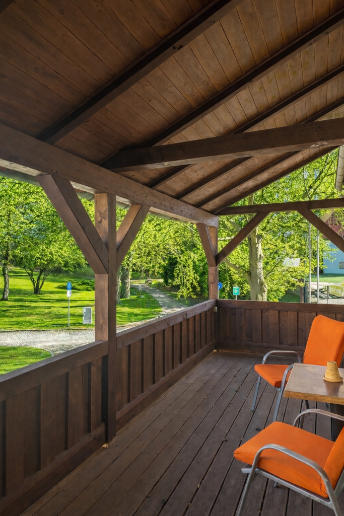 Balkon mit Holzverkleidung und orangefarbenen Stühlen, umgeben von grüner Landschaft.